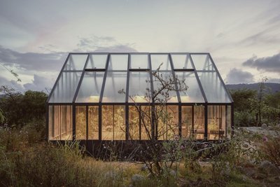 This architectural image showcases a modern greenhouse nestled within a natural landscape. The struc
