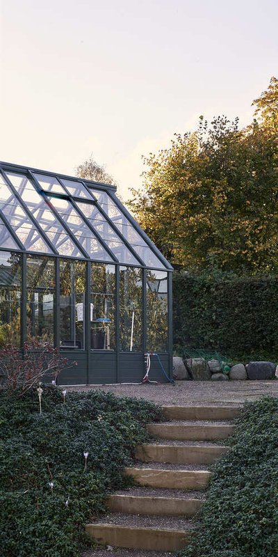 This image showcases a greenhouse nestled within a lush garden setting. The greenhouse features a gl