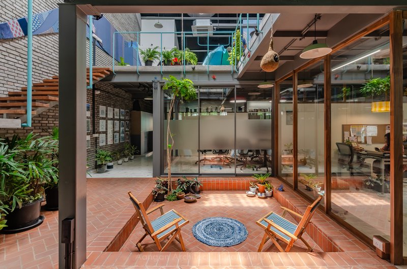 Central courtyard with terracotta floor and folding chairs surrounded by glass walls and upper-level balconies with plants