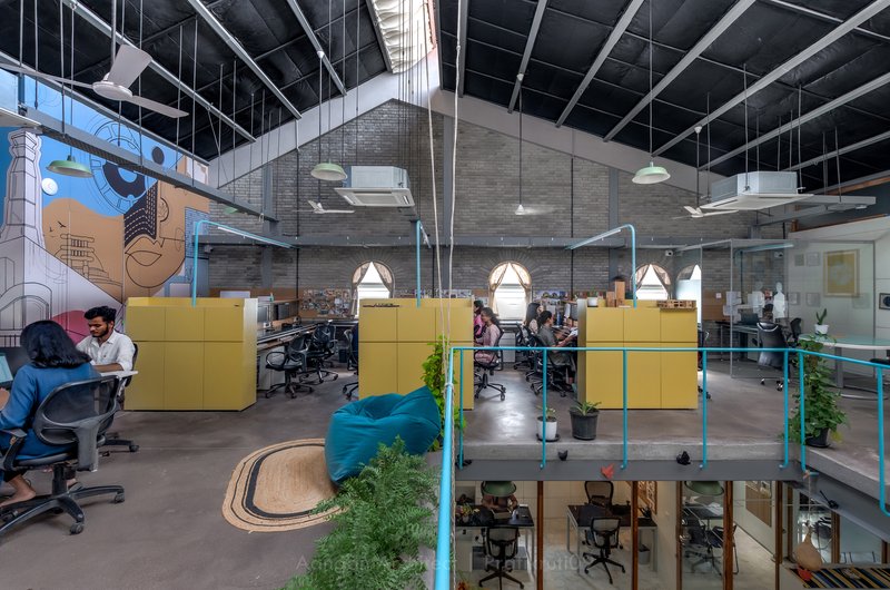 Open-plan workspace with yellow partitions and exposed black ceiling trusses under bright pendant lights