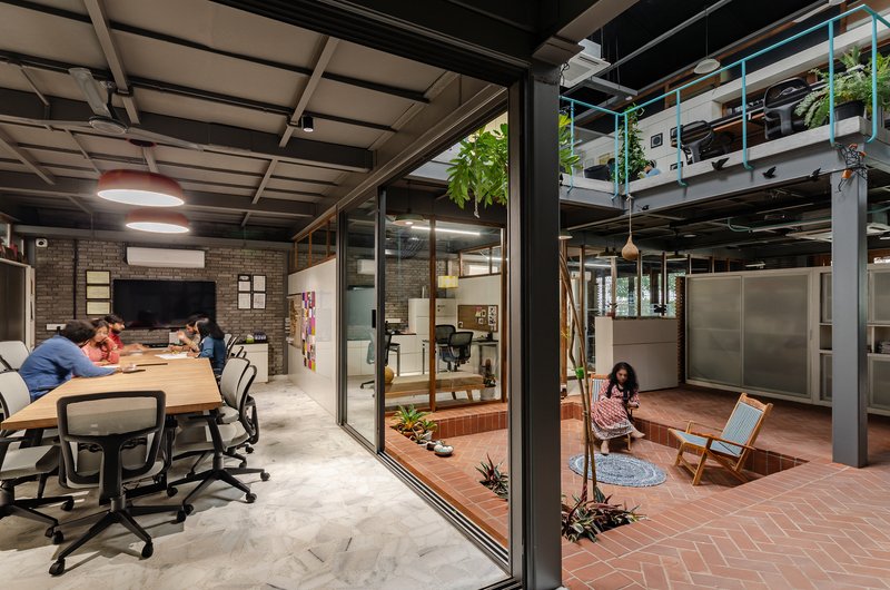 Glass-walled meeting room adjacent to sunken brick courtyard with planted trees and exposed ceiling structure