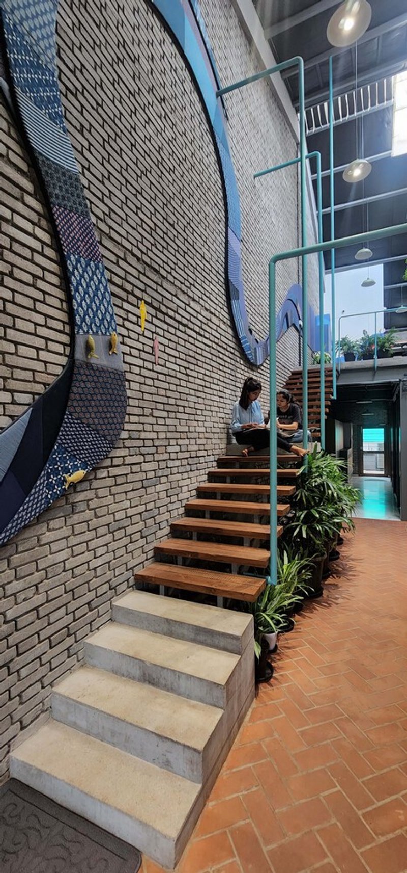 Open timber staircase ascending alongside painted brick wall mural with two people climbing the steps