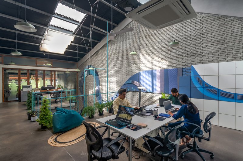 Double-height workspace with exposed brick walls, skylights, and three people working at desks