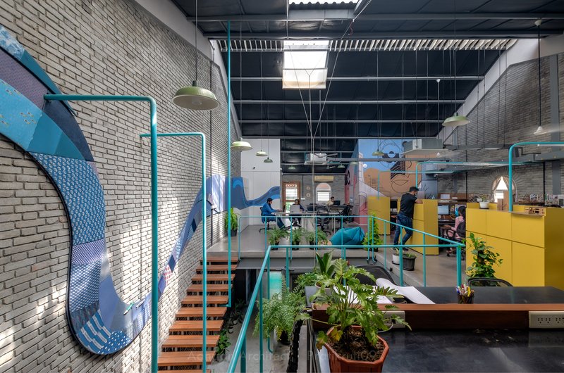 Interior view of double-height office space with painted brick murals and turquoise steel railings around mezzanine