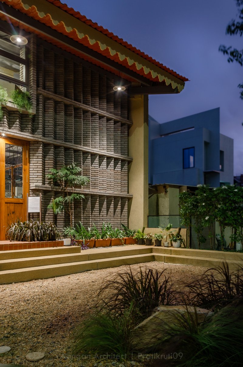 Exterior courtyard with terraced planters and horizontal brick facade under a scalloped roof at dusk