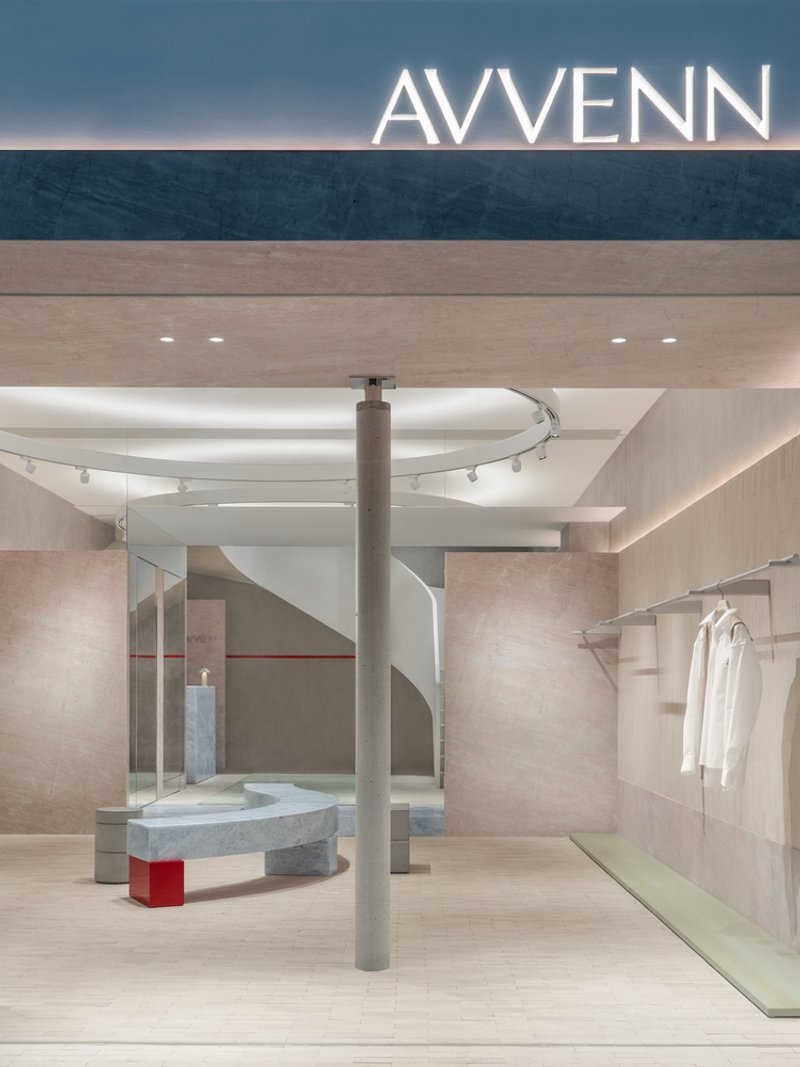 Retail interior with curved white staircase, pink stone walls, central column and curved stone seating element