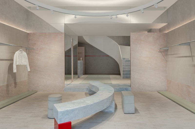 View through glass partition showing curved marble bench and spiraling staircase beneath circular skylight