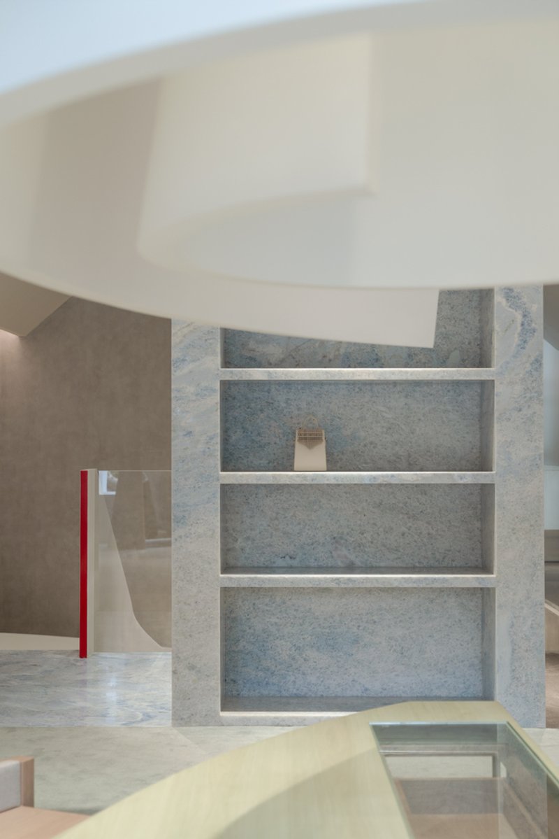 Marble shelving unit with horizontal white dividers beneath curved white soffit and recessed lighting