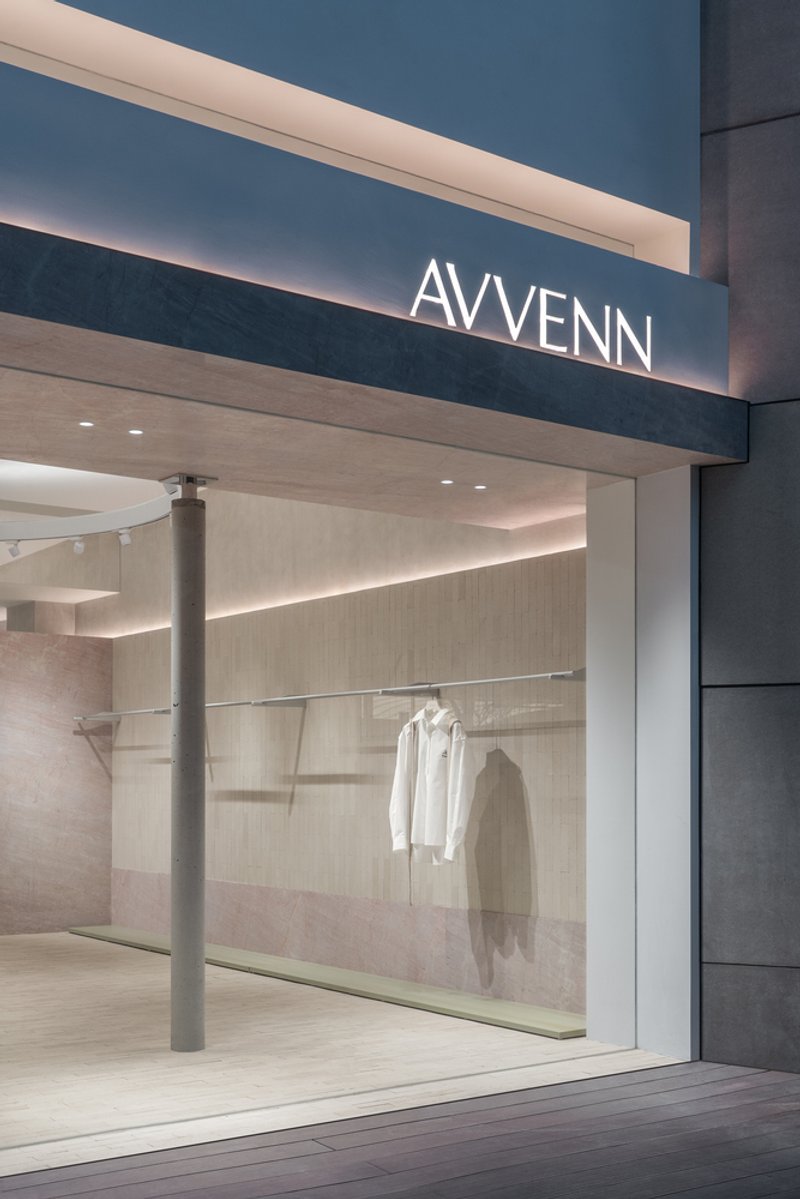 Storefront entrance at dusk with illuminated signage and view into interior with cylindrical column