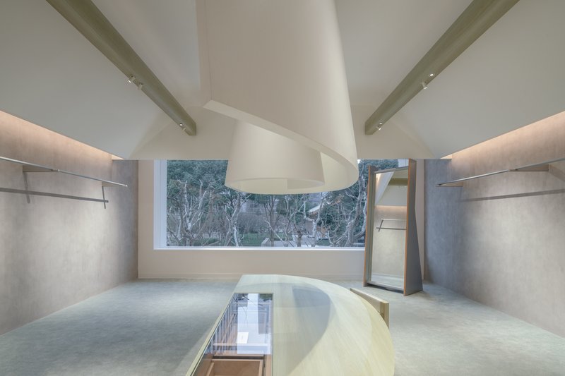 View of curved timber table with cutout beneath radial ceiling beams and backlit concrete walls