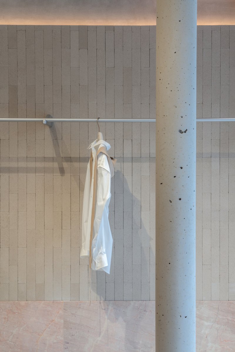 White garment hanging from a glass-enclosed display rail beside a cylindrical concrete column with tie marks
