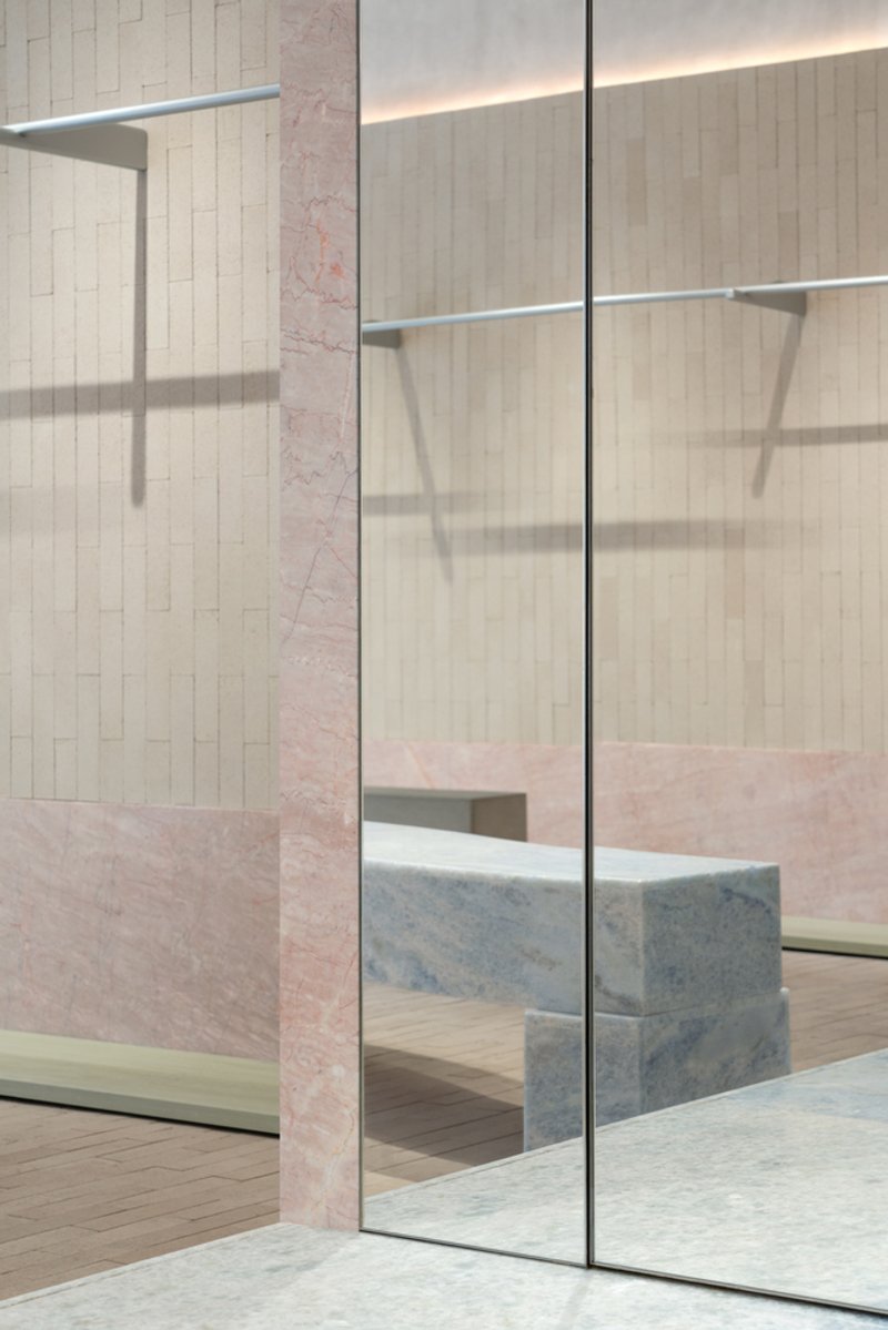 Glass display case with metal rail set against pink marble walls and pale timber paneling