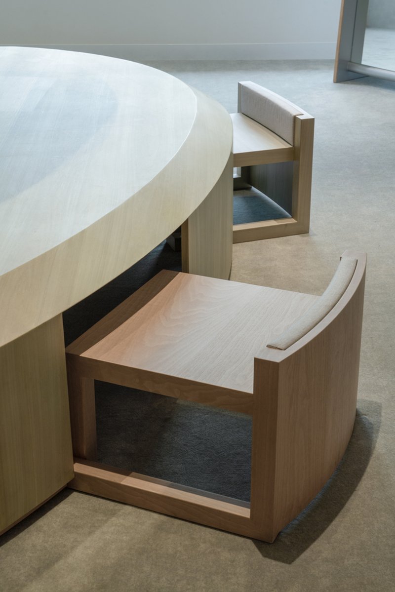 Light wood curved seating elements with integrated storage pulled out from a circular counter on a polished concrete floor