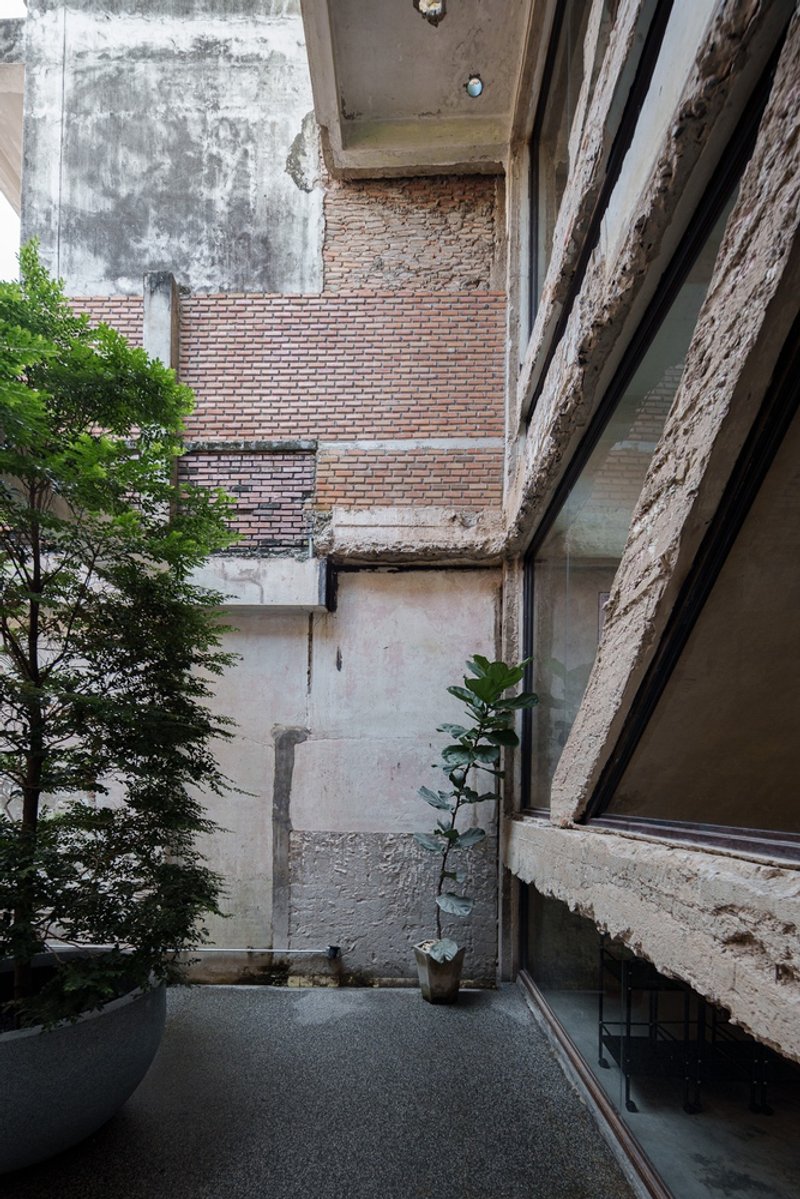 Ground floor full view: concrete bar, exposed ductwork, peeled plaster revealing brick, stair with glass balustrade, bottle display wall