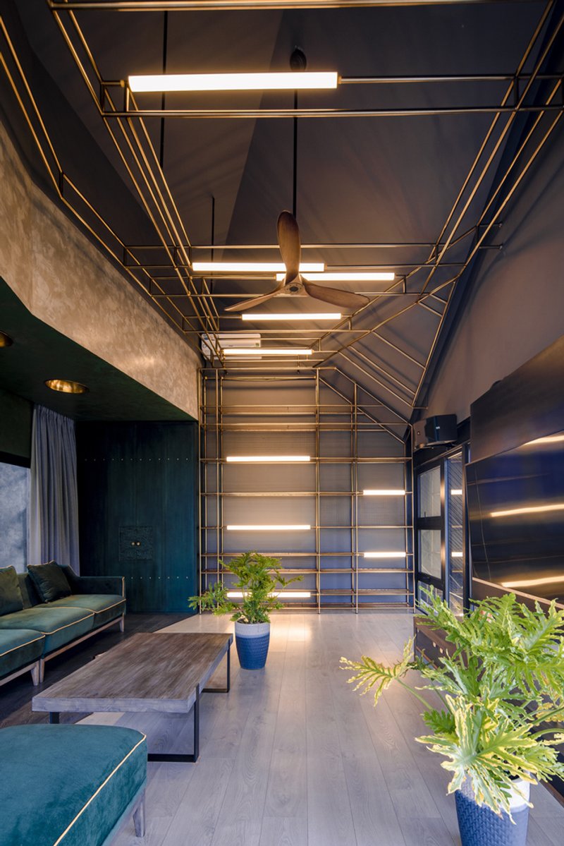 Brass geometric light frame suspended from the ceiling above a living space with potted plants