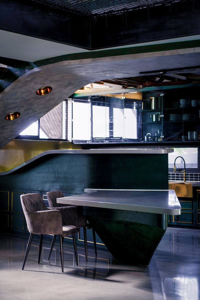 Kitchen island with dark green base and polished concrete top beneath a curved plaster ceiling with inset pendant lights