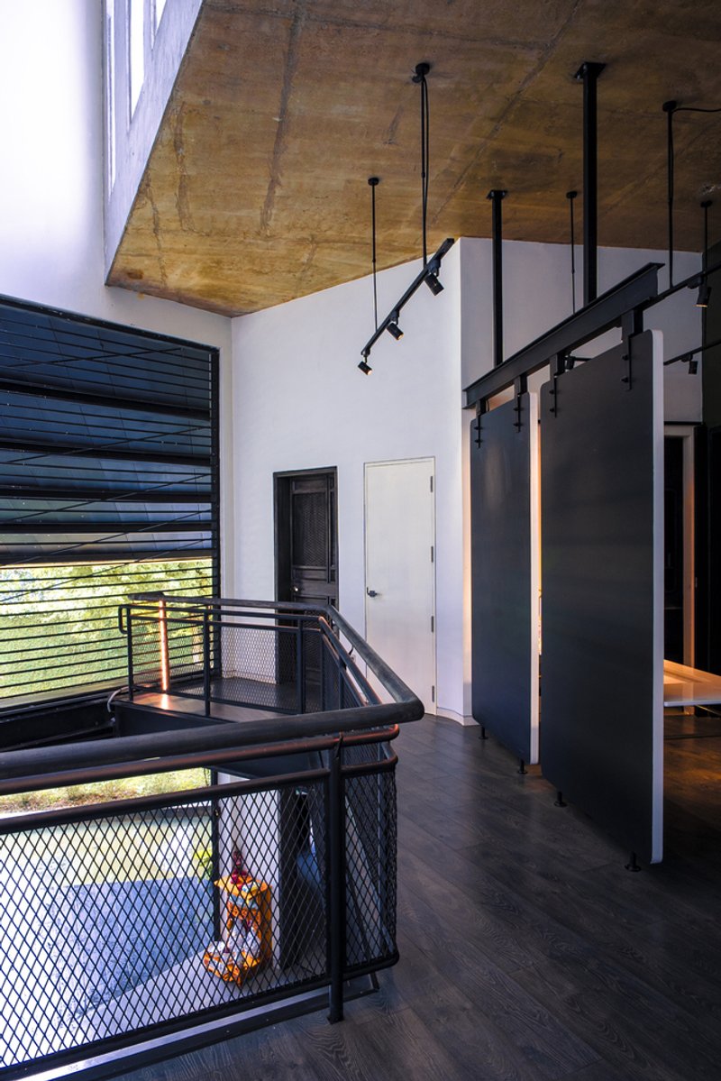 Upper landing space with exposed plywood ceiling and black pendant track lights above the mesh balustrade
