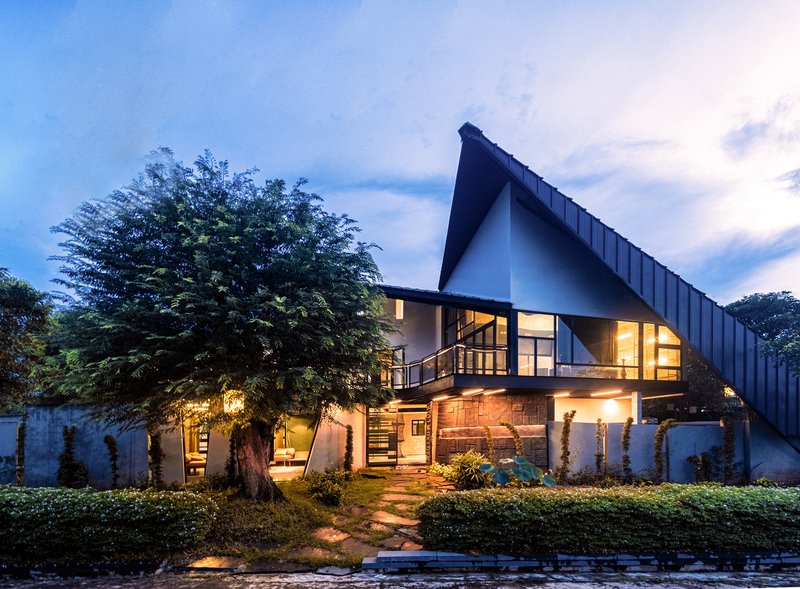 Garden elevation at twilight with large tree beside the stone base and illuminated interior spaces