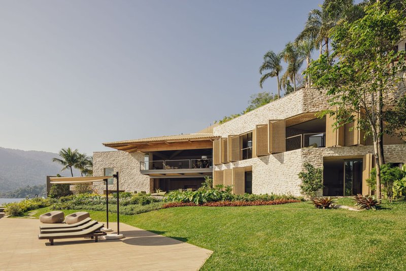 Garden view of the terraced residence with stone walls and timber louvers above manicured lawn