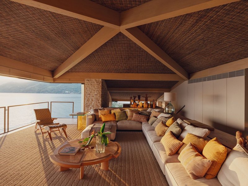 Interior living space with woven ceiling and timber beams framing views of the lake beyond