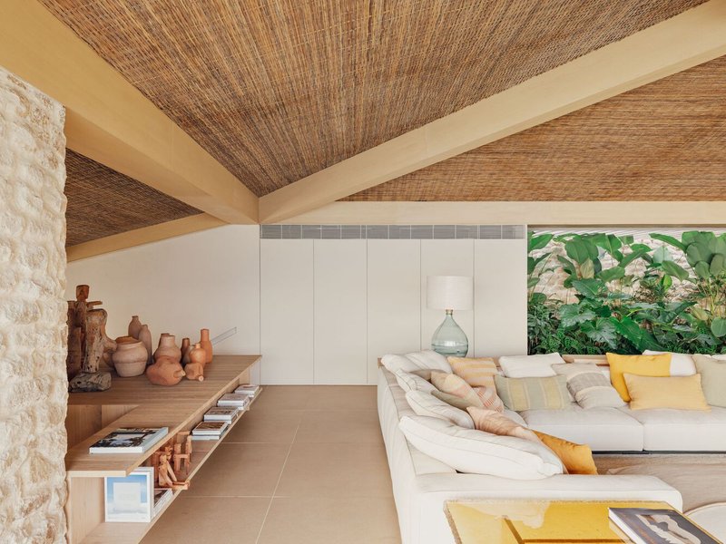 Interior with vaulted woven ceiling, white storage wall and sectional facing planted courtyard