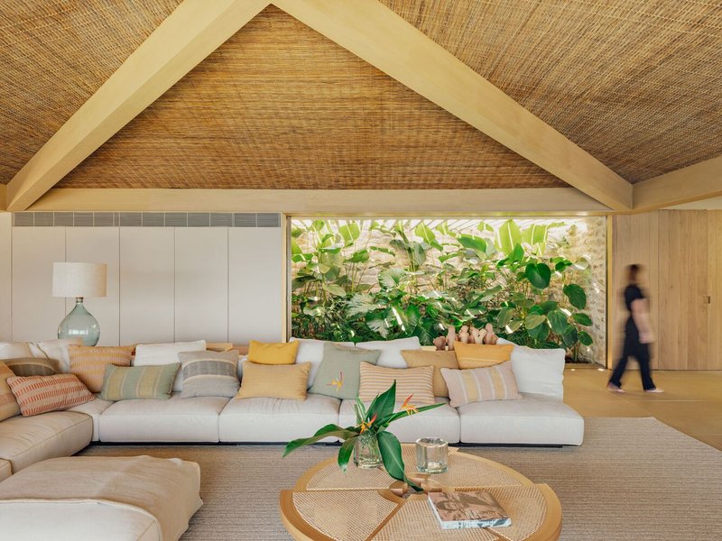Living room with woven ceiling panels and horizontal window framing planted courtyard with figure passing