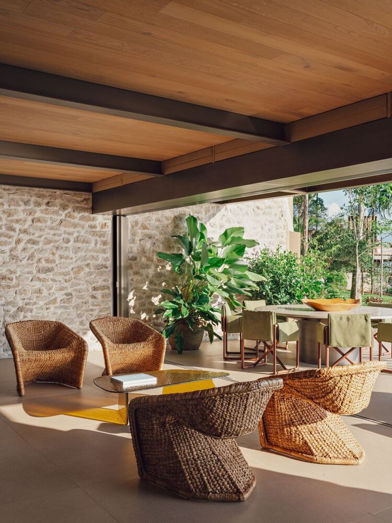 Open living space with woven seating, timber ceiling beams, stone wall, and sliding glass doors to garden