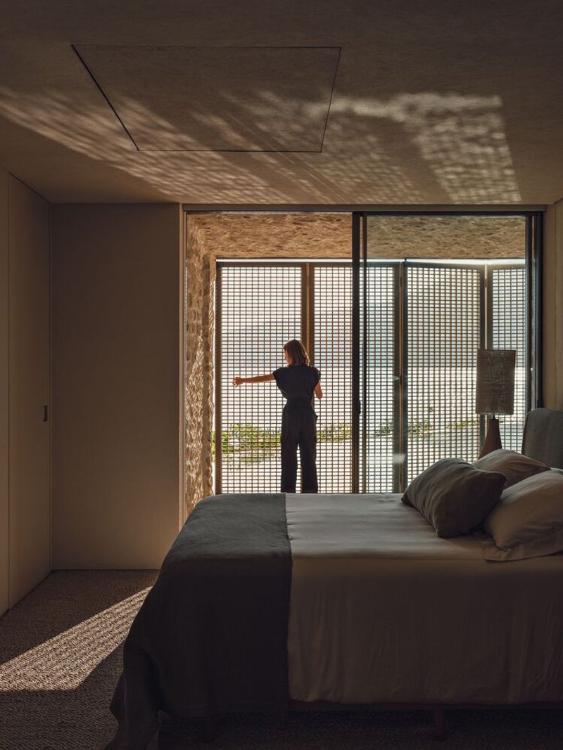 Bedroom with a person at sliding glass doors casting dappled shadow patterns across the ceiling