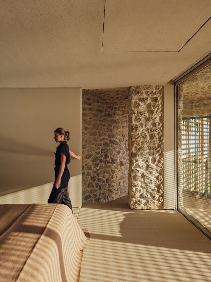 Bedroom interior with striped sunlight from the latticed screen falling across the bed and stone wall
