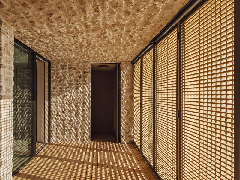 Stone-walled corridor with timber lattice screens filtering dappled light onto the floor and ceiling