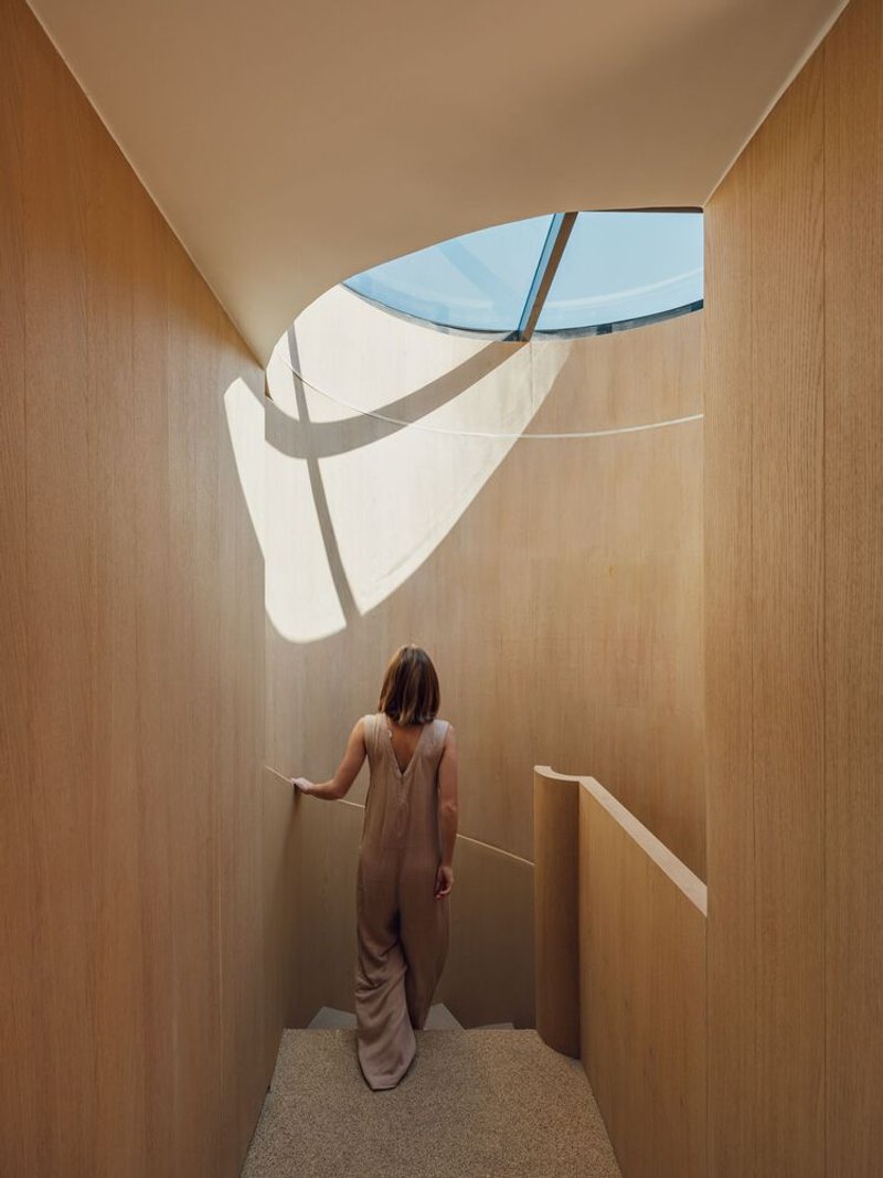 Timber-lined vestibule with curved skylight casting shadow patterns on the walls as a figure stands below