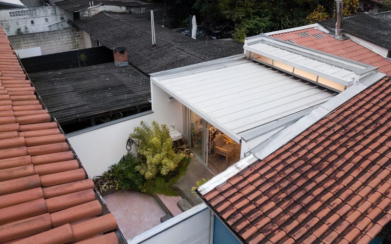 Rooftop view: translucent atelier roof between terracotta tile roofs, courtyard garden below, apartment tower beyond