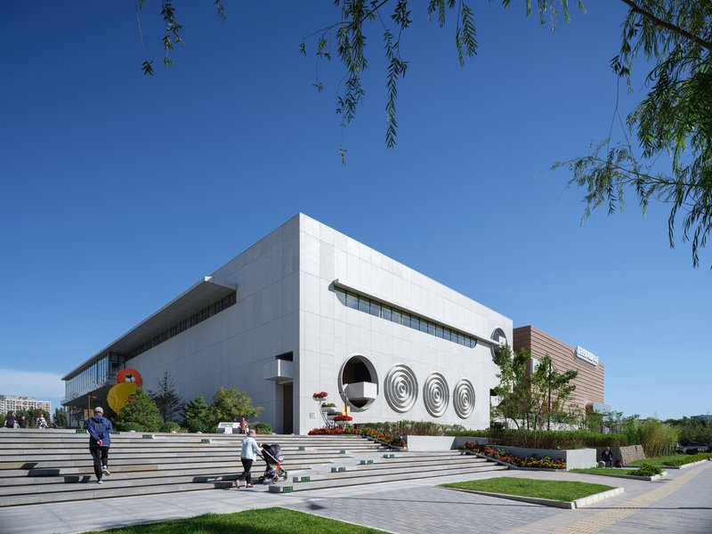 Cultural centre corner: white concrete volume with arched openings, Chinese signage, landscaped steps, pedestrians