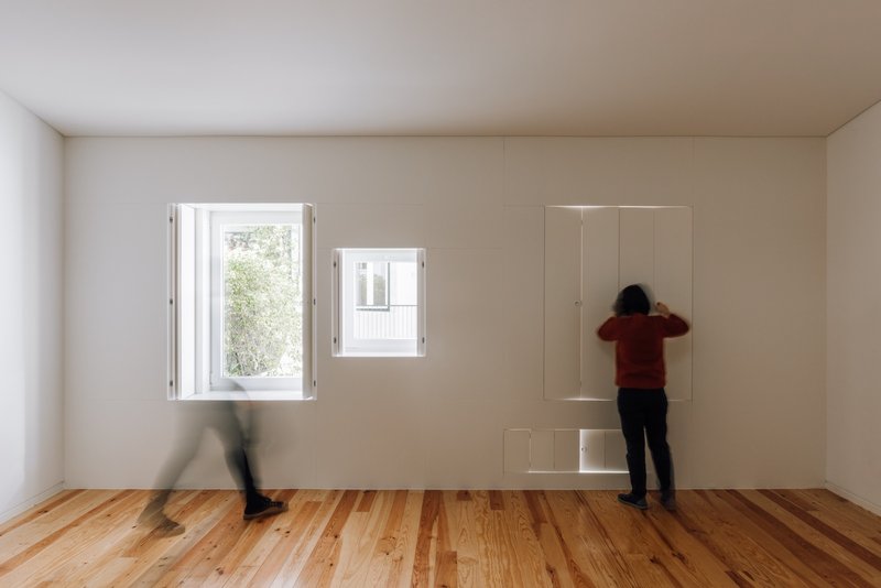White room with timber floor and flush closet doors with two people moving past open windows
