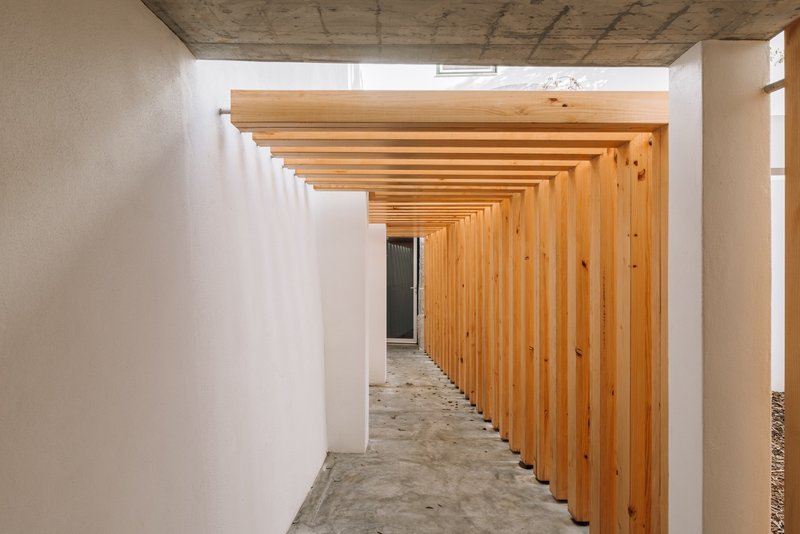 Corridor with rhythmic timber slat pergola and white walls under an exposed concrete ceiling