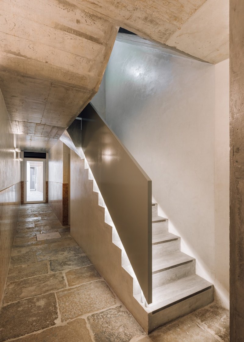 Concrete staircase with curved metal balustrade and integrated lighting beneath exposed ceiling beams