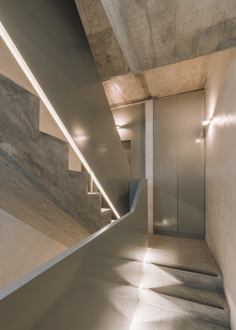 Stairwell with concrete treads, linear light slot, and curved metal guard at the landing