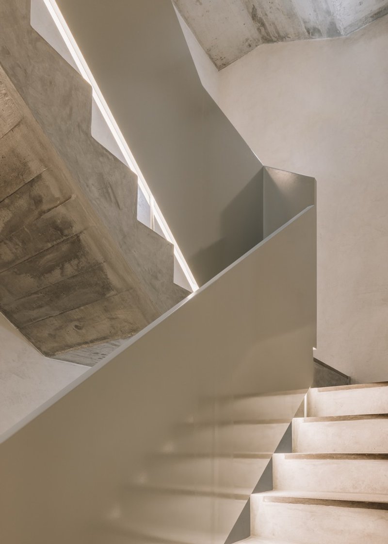 Upward view of folded concrete staircase with continuous light slot and curved white wall