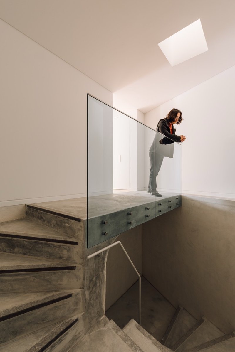Concrete staircase landing with glass guardrail and person standing under a rectangular skylight