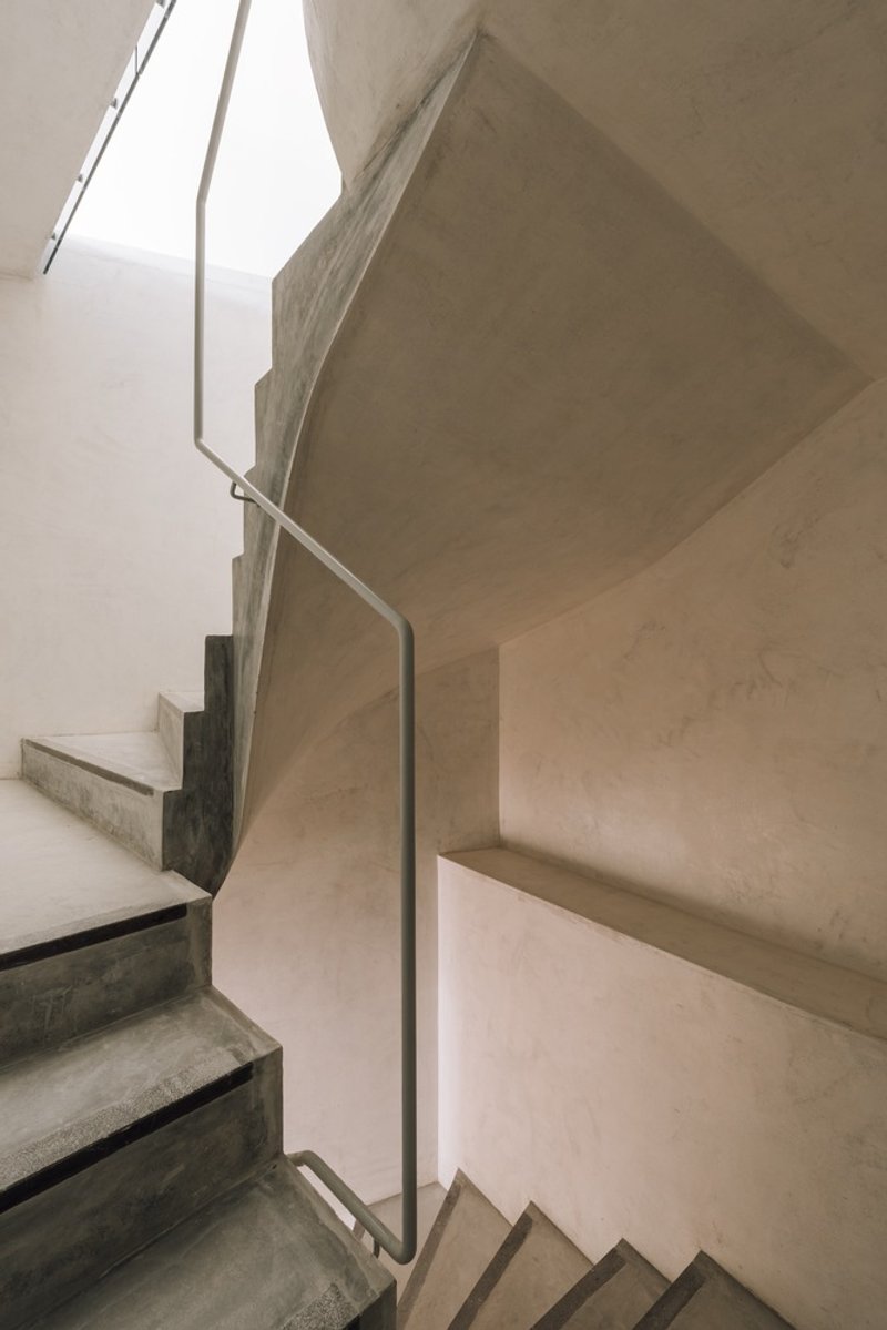 Upward view of concrete stairs with steel handrail and narrow skylight above