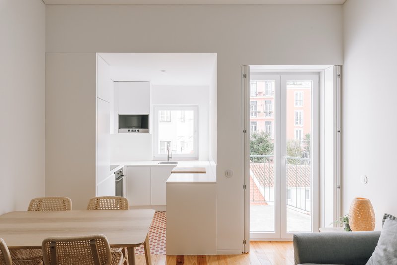 Open plan living space with white kitchen, timber dining table, and doors to exterior terrace