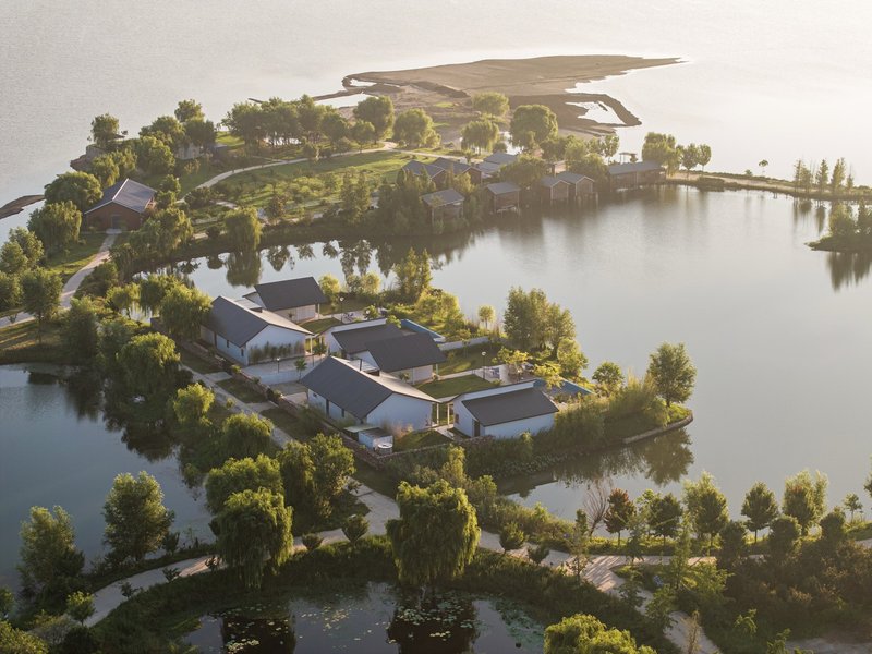 Aerial view of clustered gabled pavilions surrounded by water channels and trees in golden hour light
