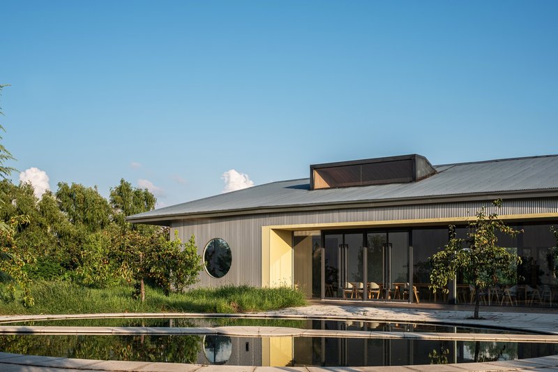 Poolside view of the corrugated metal pavilion with circular window reflected in still water