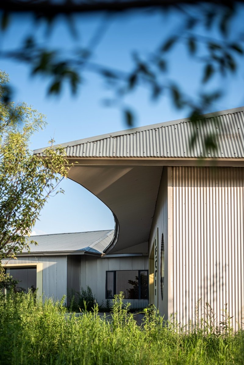 Curved roof overhang supported by angular column amid wildflowers and foliage