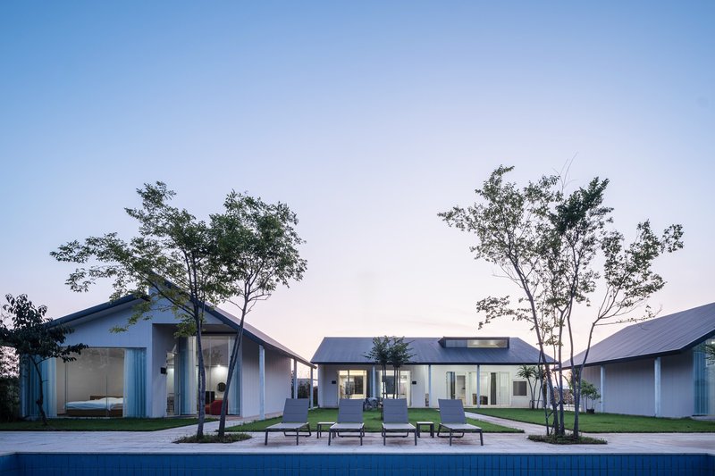 Courtyard with pool and lounge chairs between gabled pavilions framed by young trees at dusk