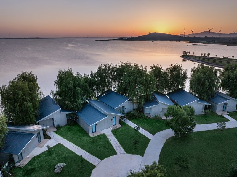 Aerial view of gabled structures with dark roofs set on lawn beside a lake at sunset