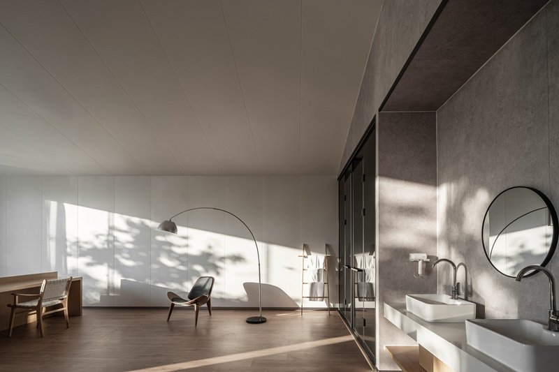 Bathroom with concrete wall, round mirror and white basin flooded with afternoon sunlight and shadows