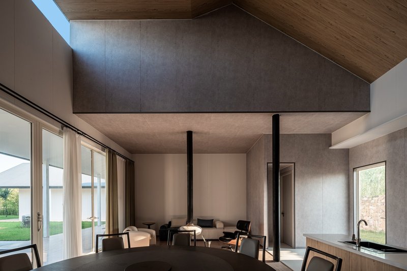 Open plan living space with concrete ceiling planes, timber volume above, and floor-to-ceiling glazing overlooking lawn