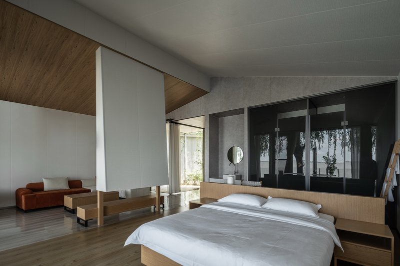 Bedroom with timber ceiling insert, concrete walls, and black framed glazing reflecting garden foliage