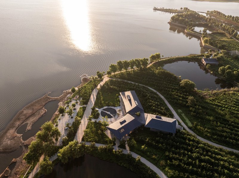 Drone view of white roofed complex nestled on a waterfront spit with vineyard terraces at golden hour